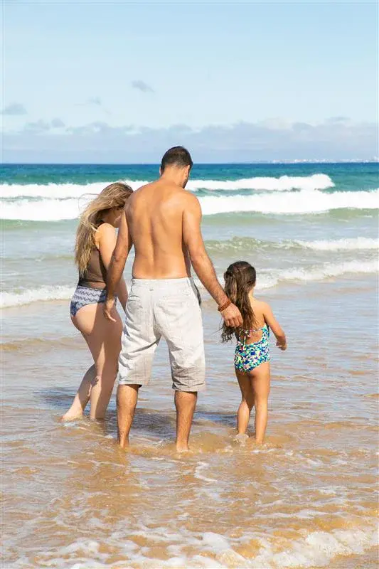 parents-little-girl-swimsuits-walking-ankle-deep-ocean-waves